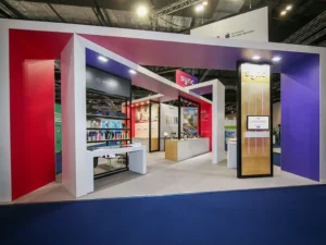 An angular, bespoke exhibition stand for Sync at the Bett Show, with overhead panel structures in red and purple, product displays and digital displays.
